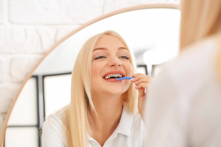 young woman metal braces toothbrush home - How to Floss with Braces in Twinsburg, OH