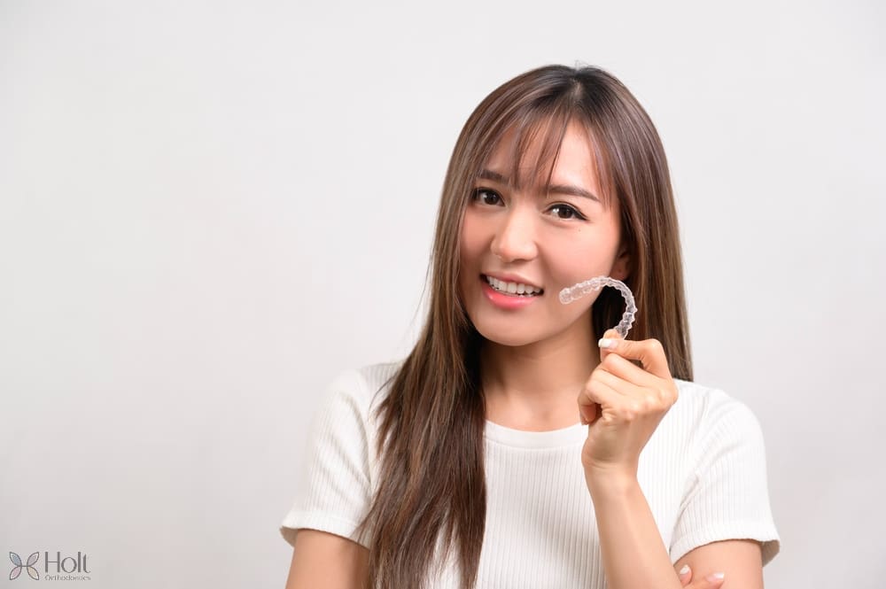 young smiling woman holding invisalign clear aligners white background - How Does Invisalign Work in Twinsburg, OH 